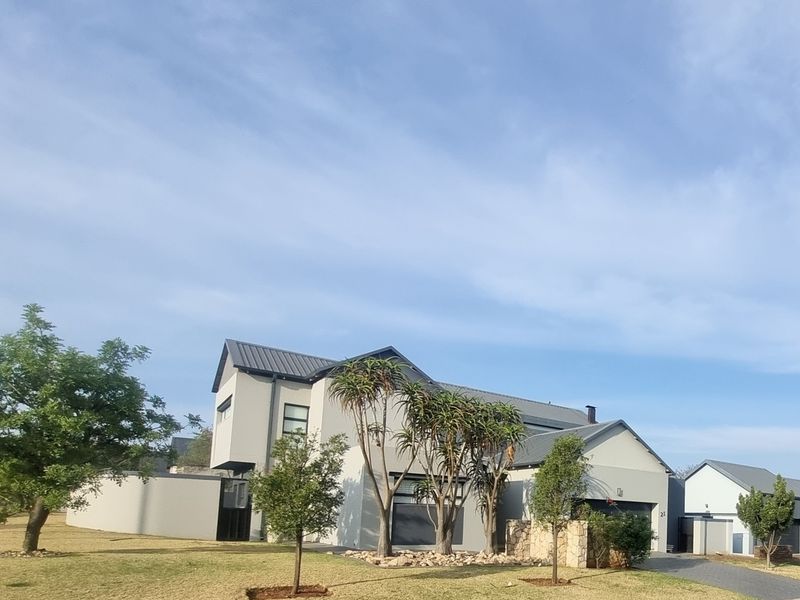 Modern double-story residential home featuring a metal roof, stone cladding accents, and a paved driveway with established landscaping.
