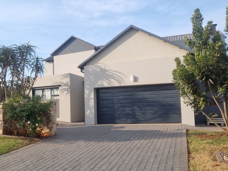 Front elevation of a modern house featuring a paved driveway, double garage, and stone-accented landscaping.
