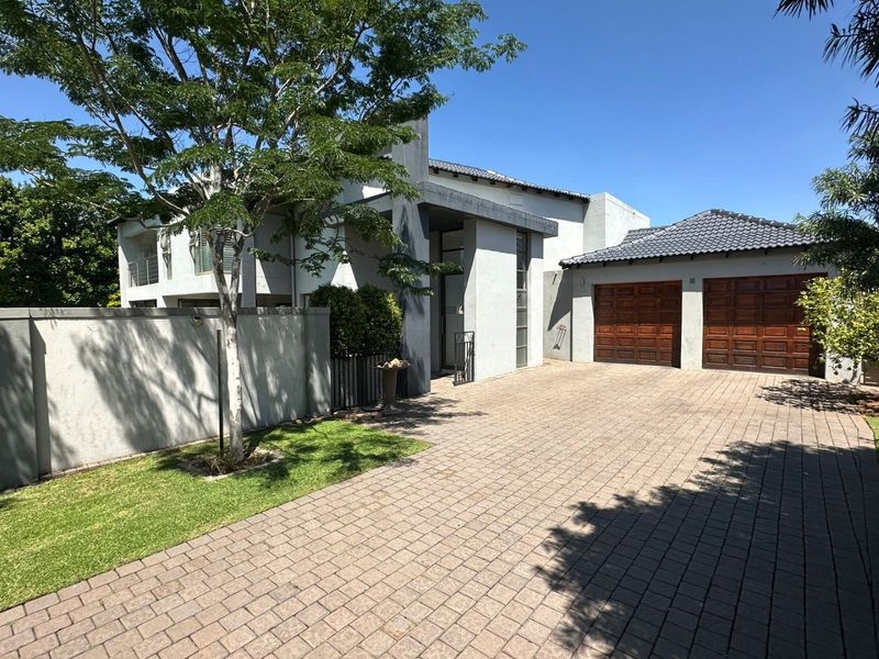Front elevation of a modern house featuring a paved driveway, double wooden garage doors, and a well-maintained boundary wall.