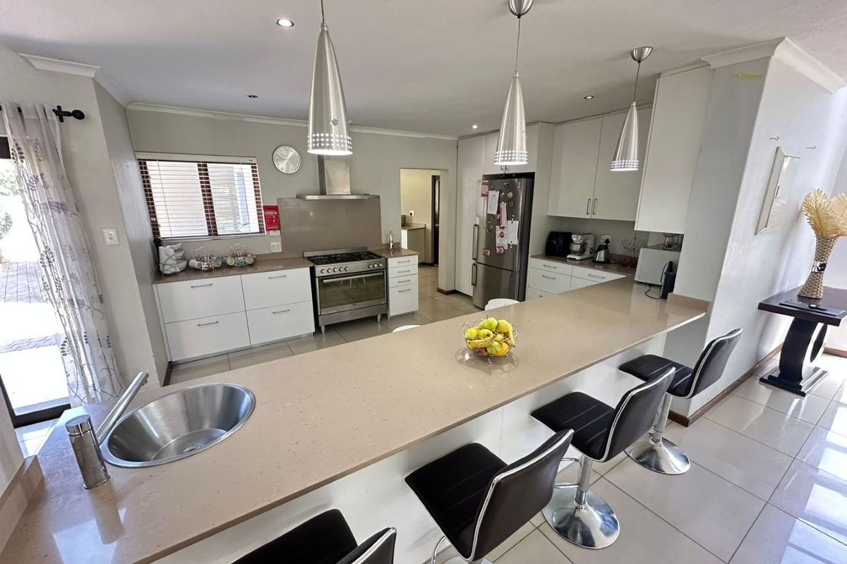 Modern kitchen featuring a large stone breakfast bar, stainless steel sink, gas stove with extractor fan, and ample built-in cabinetry with tiled flooring.