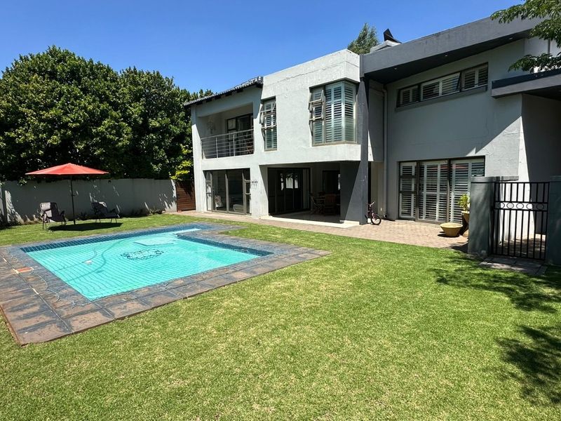 Rear view of the property featuring a swimming pool, paved patio area, covered ground floor terrace, and an upper-level balcony with metal railings.