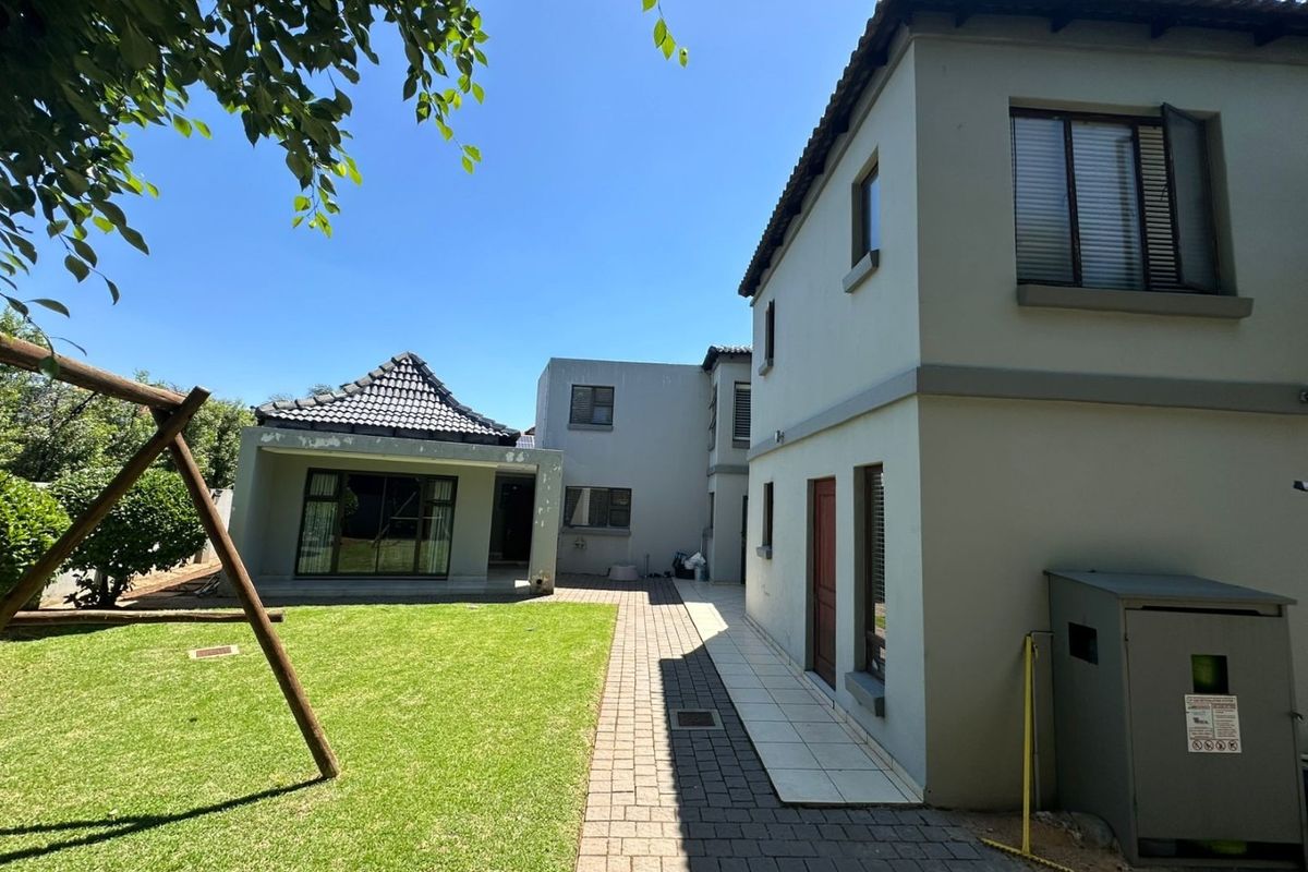 Rear view of the property featuring a paved walkway, lawn area, and multi-story building structure with tiled roofing and aluminium window frames.
