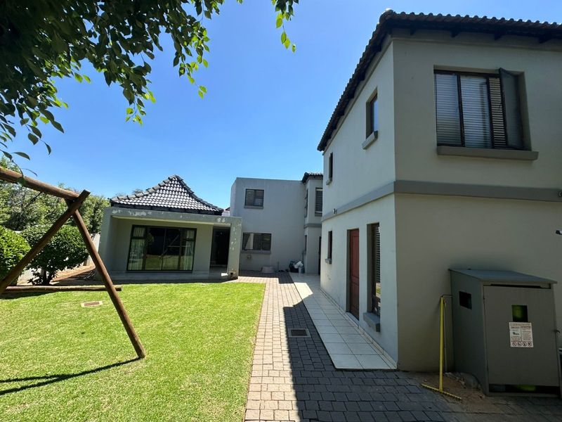 Rear view of the property featuring a paved walkway, lawn area, and multi-story building structure with tiled roofing and aluminium window frames.