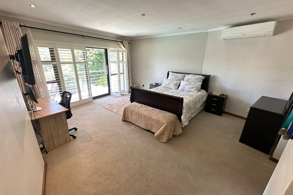 Spacious bedroom featuring carpet flooring, recessed downlights, a wall-mounted air conditioner, and plantation shutters opening to an outdoor area.
