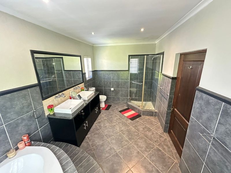 Spacious bathroom featuring a double vanity with vessel sinks, a corner shower enclosure, and a built-in bathtub with dark grey tiled finishes.
