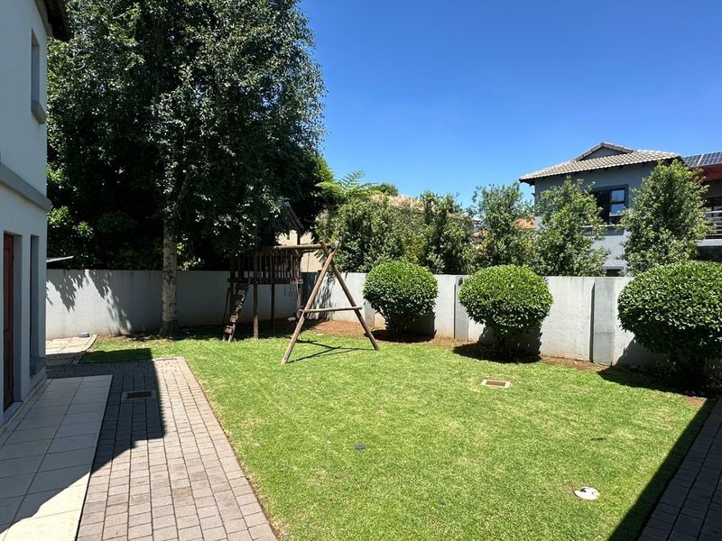A well-maintained rear garden featuring a paved walkway, manicured lawn, and secure perimeter walling, providing a private outdoor space.