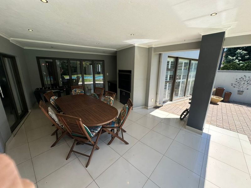Spacious covered patio featuring tiled flooring, recessed lighting, and a built-in braai, providing a seamless transition to the outdoor garden and pool area.