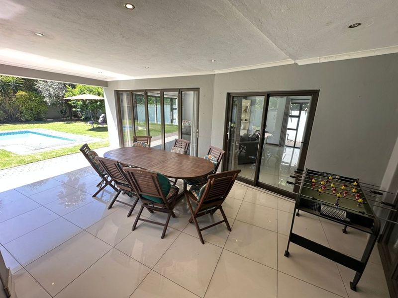 A spacious covered patio featuring large format floor tiles, recessed lighting, and sliding glass doors that provide seamless access to the garden and pool area.