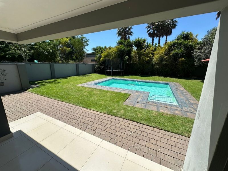 A well-maintained outdoor area featuring a swimming pool, paved patio space, and a manicured lawn enclosed by a perimeter wall.