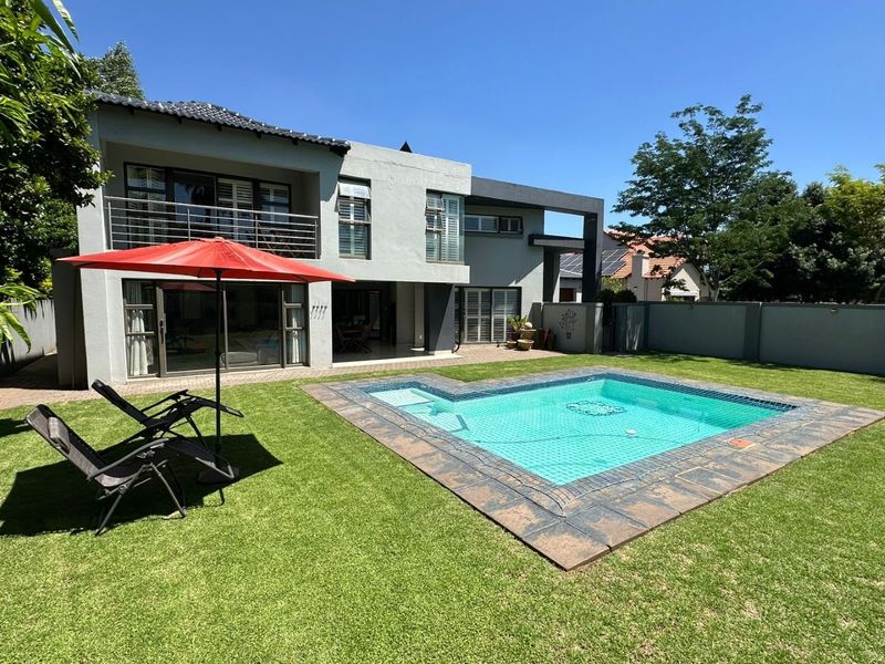 Rear view of a modern two-story house featuring a swimming pool, manicured lawn, and an upper-level balcony with metal railings.