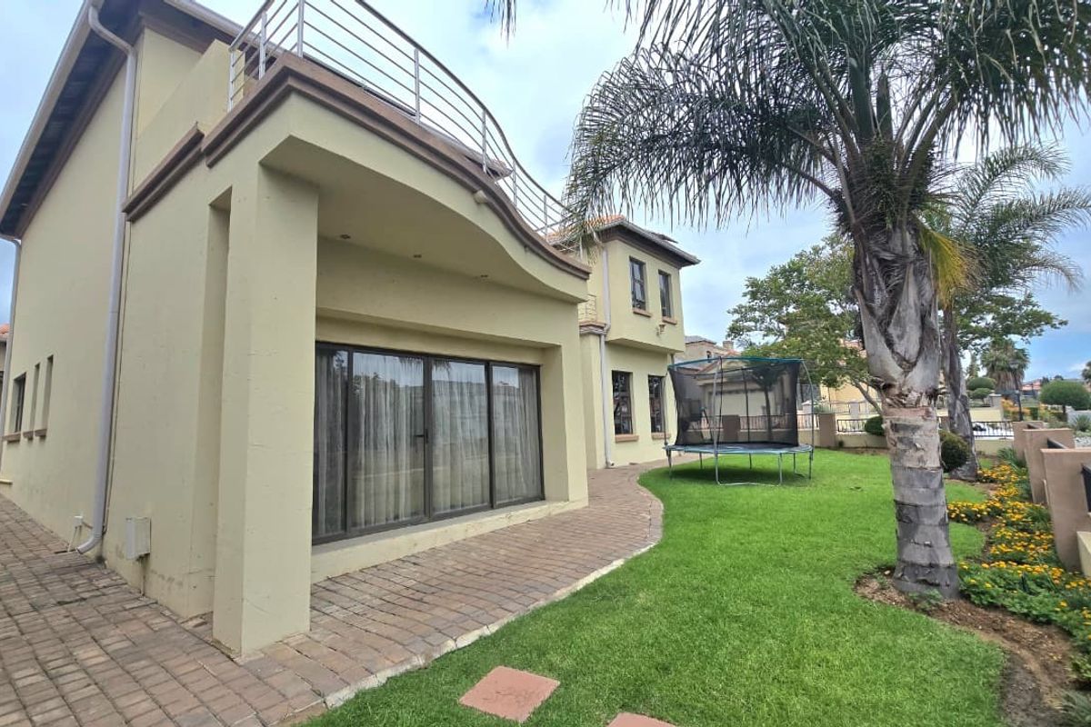 Rear view of the property featuring a paved patio, a landscaped garden, and an upper-level balcony with metal railings.