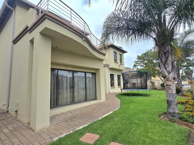 Rear view of the property featuring a paved patio, a landscaped garden, and an upper-level balcony with metal railings.