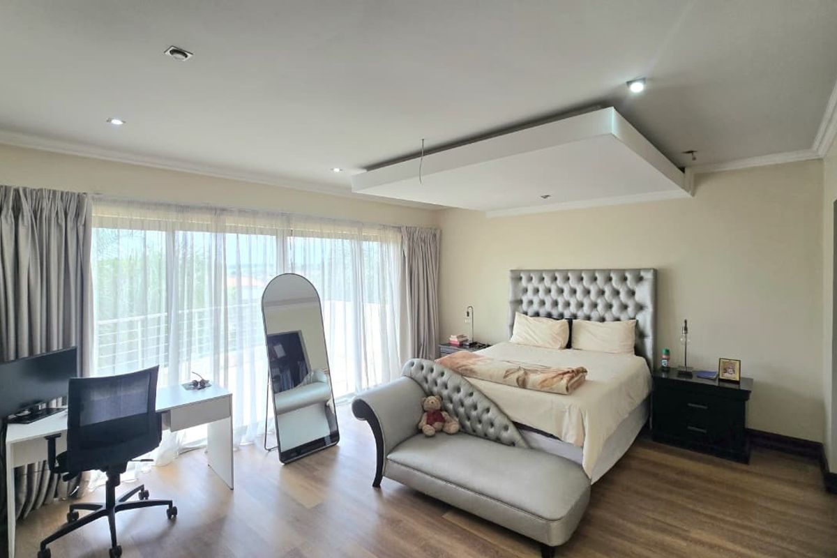 Spacious bedroom featuring modern laminate flooring, recessed ceiling detail with downlights, and large sliding glass doors providing access to an outdoor balcony.