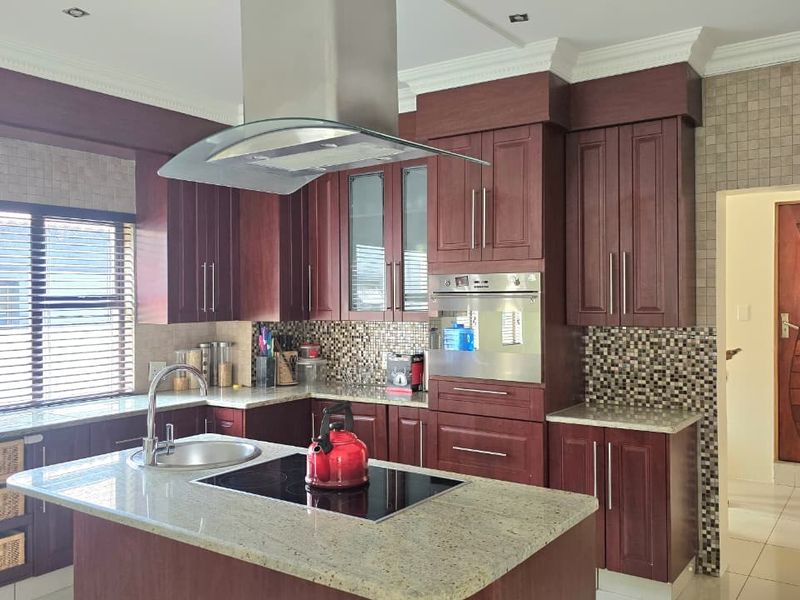 A well-appointed kitchen featuring dark wood cabinetry, granite countertops, a central island with an induction cooktop, and a modern stainless steel extractor fan.