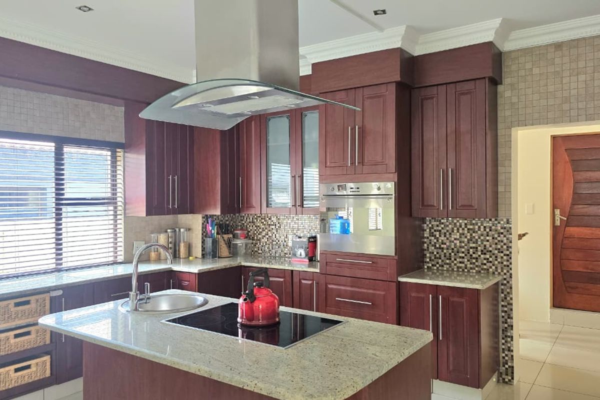 A well-appointed kitchen featuring dark wood cabinetry, granite countertops, a central island with an induction cooktop, and a modern stainless steel extractor fan.