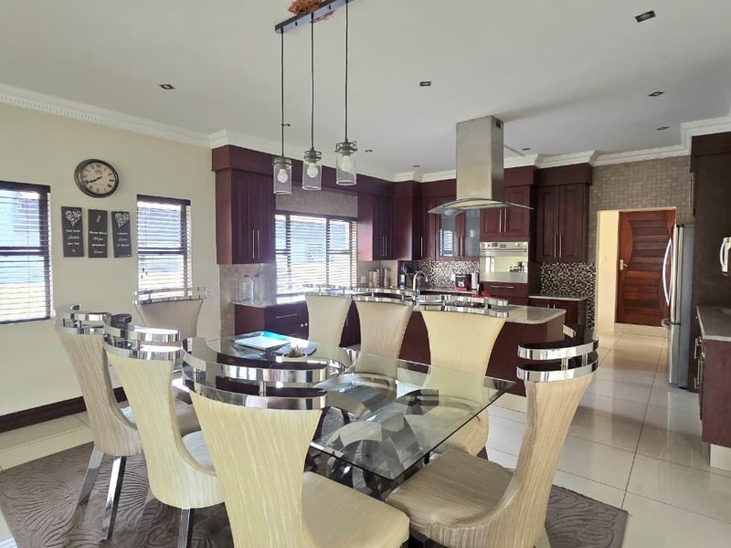 Spacious open-plan kitchen and dining area featuring dark wood cabinetry, granite countertops, modern pendant lighting, and polished tile flooring throughout.