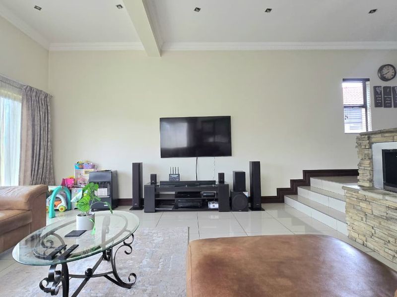 Spacious living room featuring tiled flooring, recessed downlights, and a prominent stone-clad fireplace, with direct access to outdoor areas via sliding glass doors.