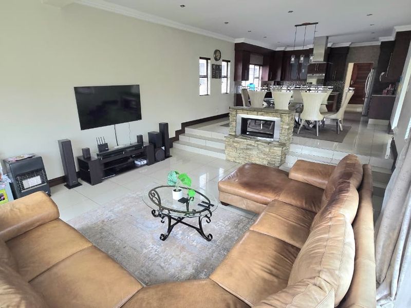 Spacious open-plan living and dining area featuring tiled floors, a central stone-clad fireplace, and a modern kitchen with dark cabinetry.