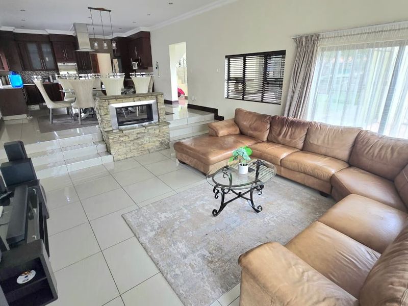 Spacious open-plan living and kitchen area featuring tiled floors, a central stone-clad fireplace, and direct access to the outdoor space through sliding doors.