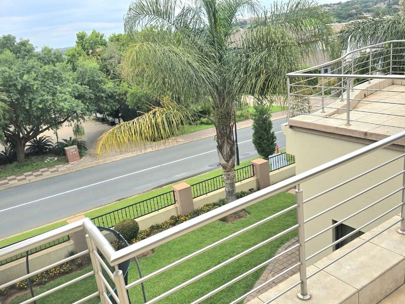A spacious elevated balcony featuring modern stainless steel balustrades and tiled flooring, overlooking the front garden and street.