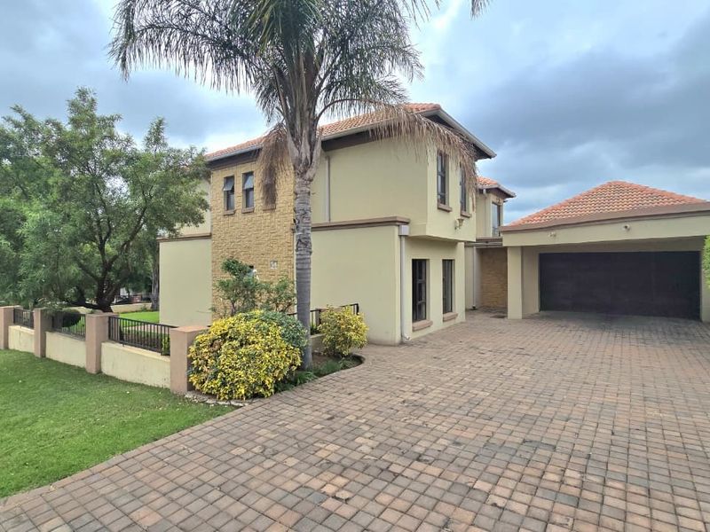 Front view of a double-story residential property featuring a paved driveway, double garage, and landscaped garden with stone cladding accents.