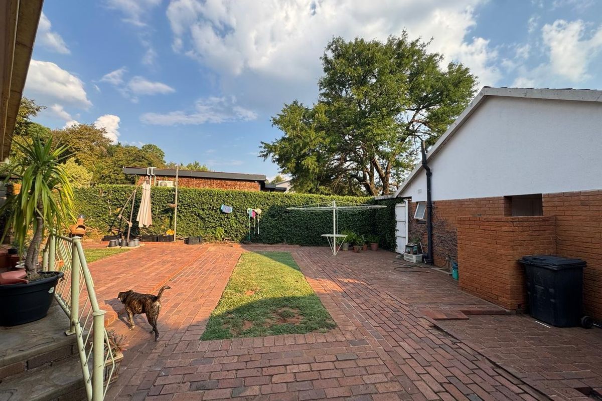 A spacious rear garden featuring extensive brick paving, a central lawn strip, and established perimeter hedging, providing a private outdoor area.