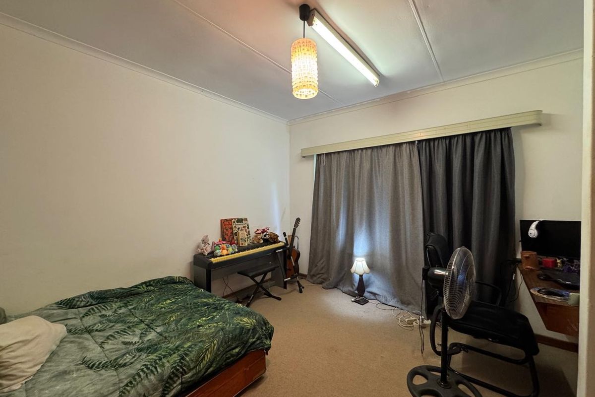 A functional bedroom featuring neutral walls, carpeted flooring, and a window dressed with full-length curtains.