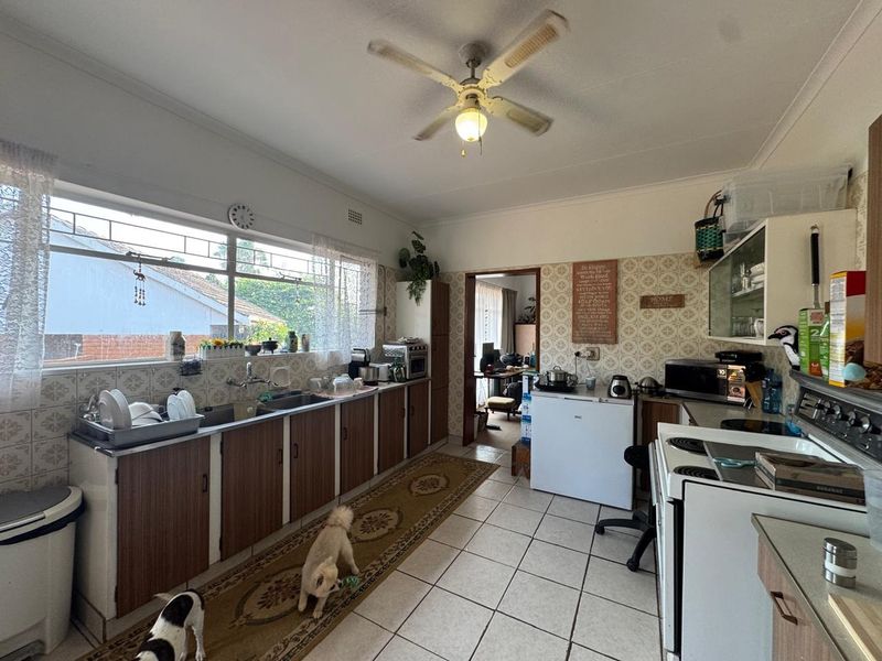 A functional kitchen featuring tiled flooring, built-in cabinetry, a double basin sink, and a ceiling fan, offering potential for modern updates.