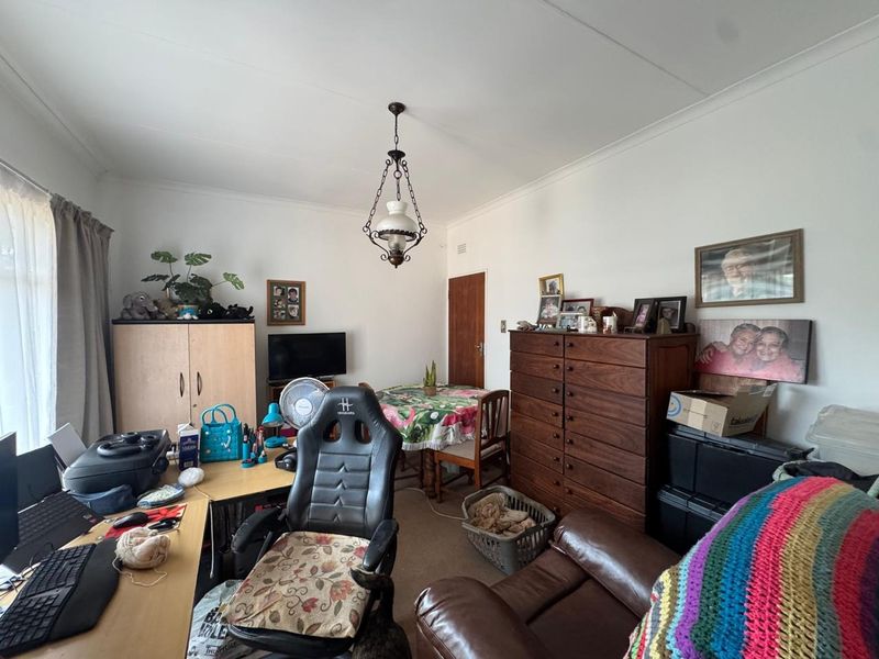 A multi-purpose living area featuring a coved ceiling and a classic pendant light fixture, currently utilized as a combined lounge and home office space.