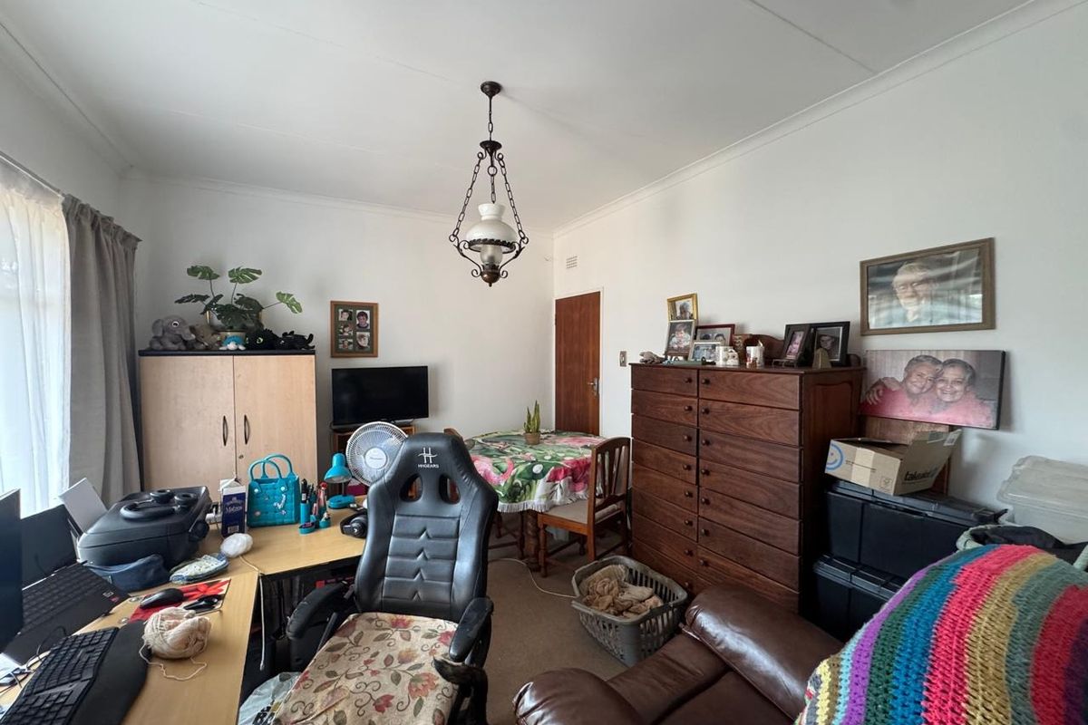 A multi-purpose living area featuring a coved ceiling and a classic pendant light fixture, currently utilized as a combined lounge and home office space.