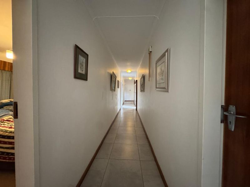 A long, neutral-toned hallway featuring tiled flooring and multiple internal door access points, connecting various rooms within the home.