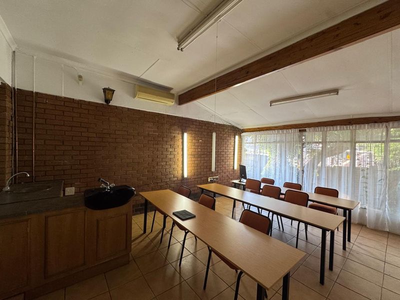 A functional office or workspace featuring exposed brick walls, timber ceiling beams, tiled flooring, and a small built-in kitchenette area.