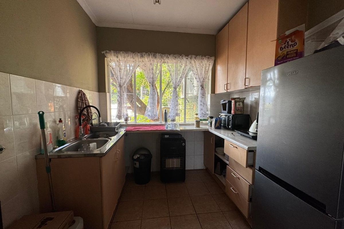A functional kitchen featuring laminate cabinetry, tiled splashbacks, and tiled flooring, offering a practical layout with natural light from the window.