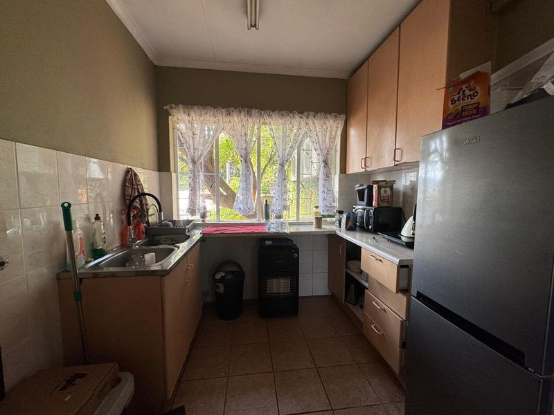 A functional kitchen featuring laminate cabinetry, tiled splashbacks, and tiled flooring, offering a practical layout with natural light from the window.