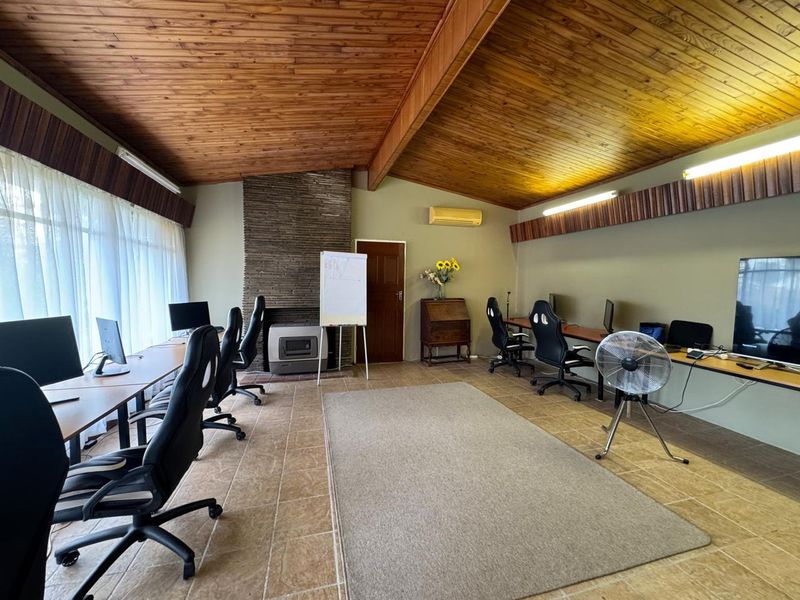 Spacious office area featuring a vaulted wood-paneled ceiling, stone-clad fireplace with a wood-burning stove, tiled flooring, and built-in desk workstations.