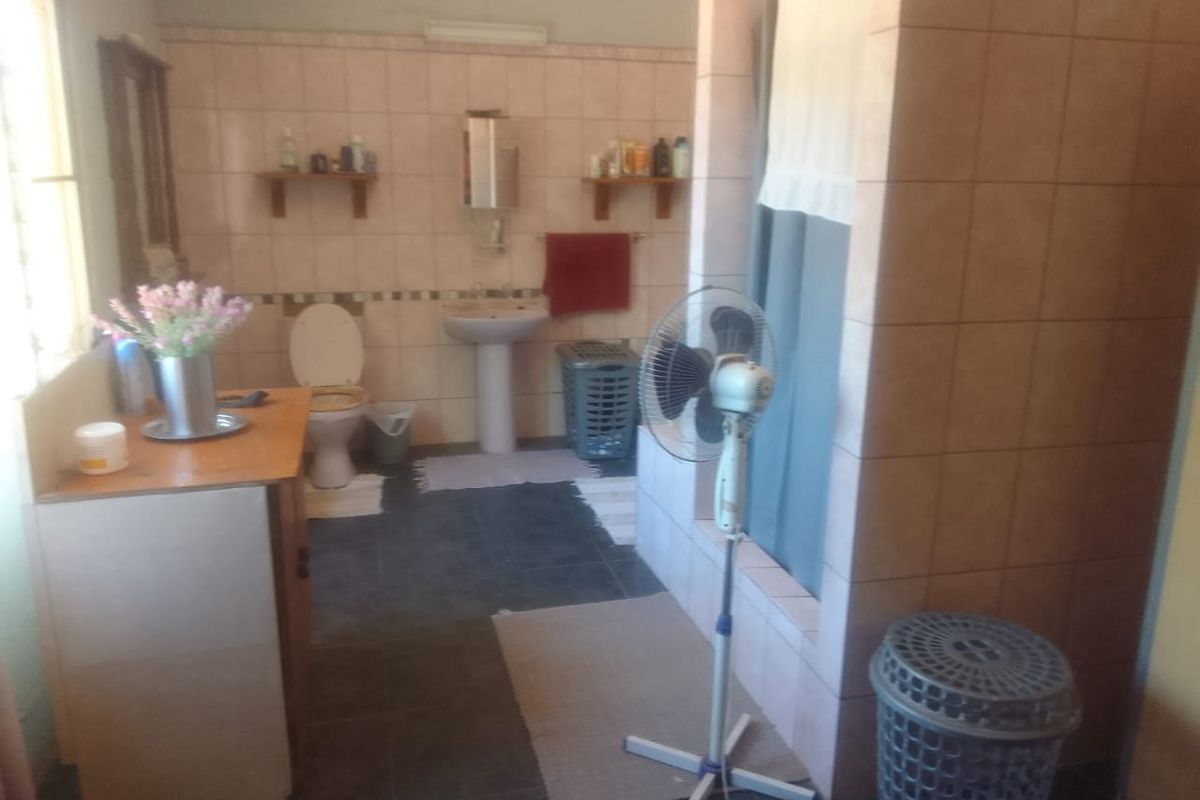A dated bathroom featuring a pedestal washbasin, toilet, and a tiled shower enclosure with neutral wall tiling.