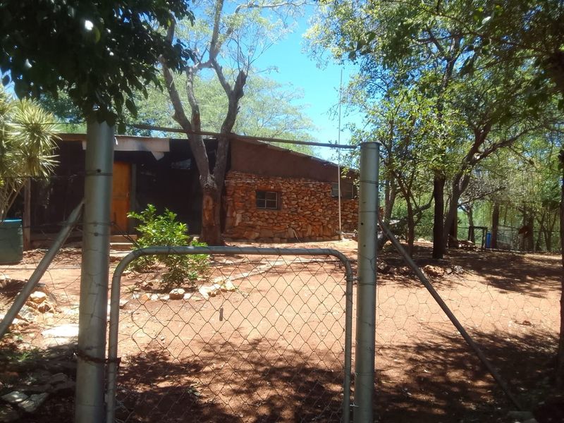 Front view of a rustic farm dwelling featuring stone masonry walls, a metal roof, and a fenced perimeter entrance.