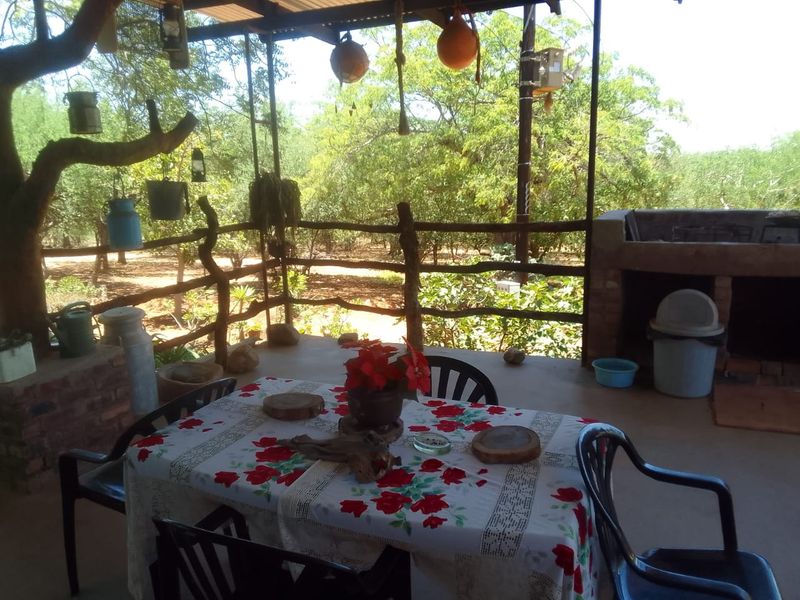 Covered outdoor patio area featuring a built-in brick braai, rustic timber railing, and views overlooking the surrounding farm landscape.