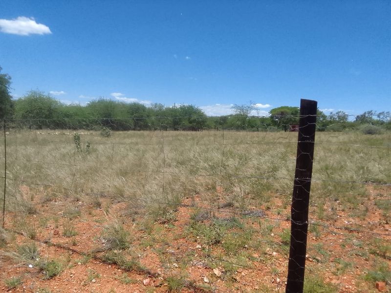 An expansive, undeveloped plot of land featuring natural grass cover and perimeter wire fencing with wooden posts.