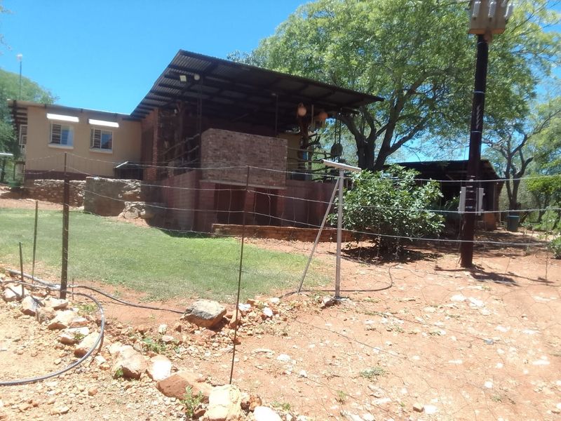 Rear view of a farm property featuring a covered patio area, brick construction, and corrugated metal roofing set within a rural landscape.