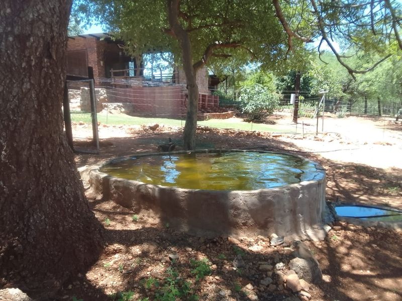 A rustic circular concrete water reservoir situated in a natural farm setting with mature trees and perimeter fencing.