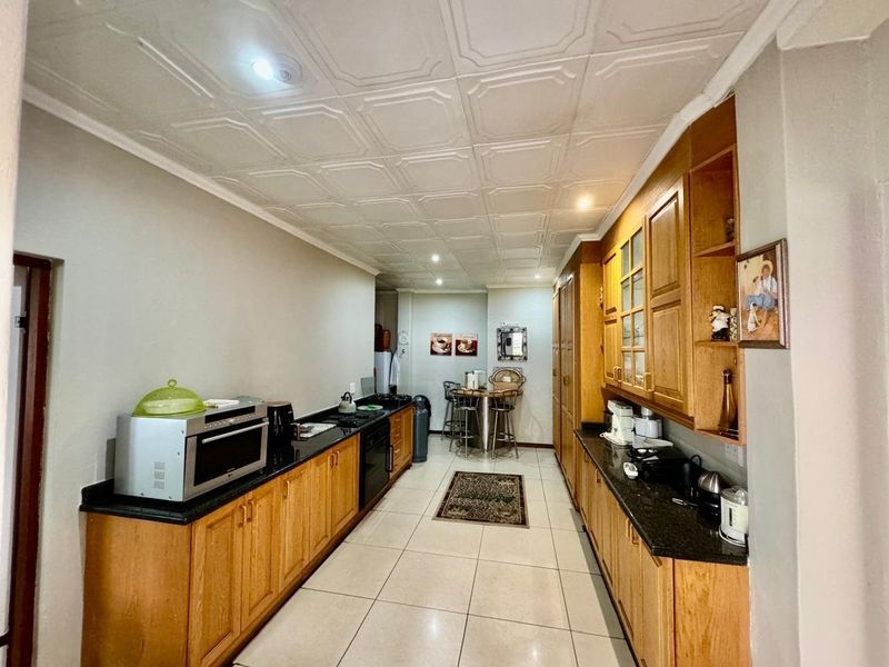 A functional galley-style kitchen featuring warm wooden cabinetry, granite countertops, built-in cooking appliances, and a distinctive coffered ceiling design.