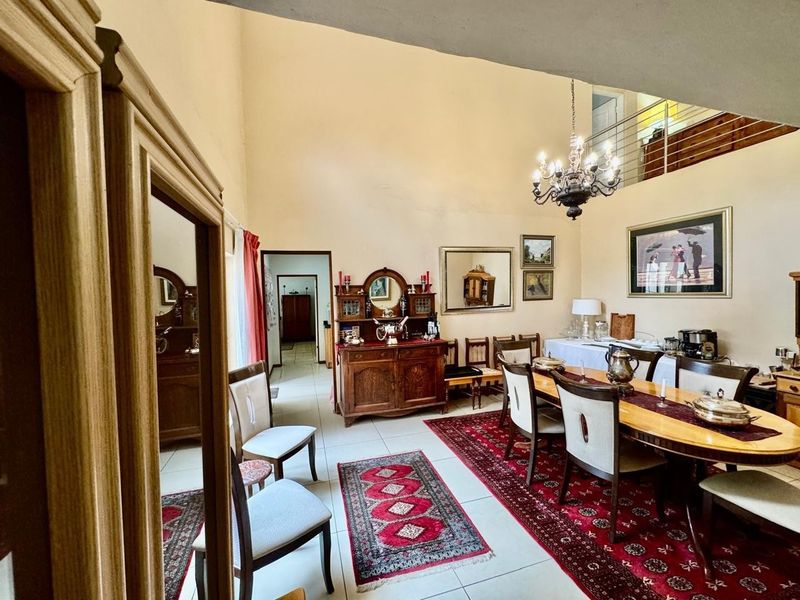 Spacious dining area featuring a high vaulted ceiling, elegant chandelier, and tiled flooring, with an open view to the upper mezzanine level.