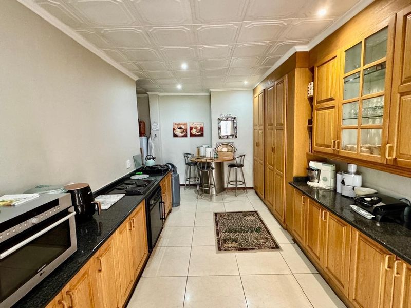 A functional kitchen featuring extensive wooden cabinetry, dark granite countertops, built-in cooking appliances, and decorative ceiling tiles with tiled flooring throughout.