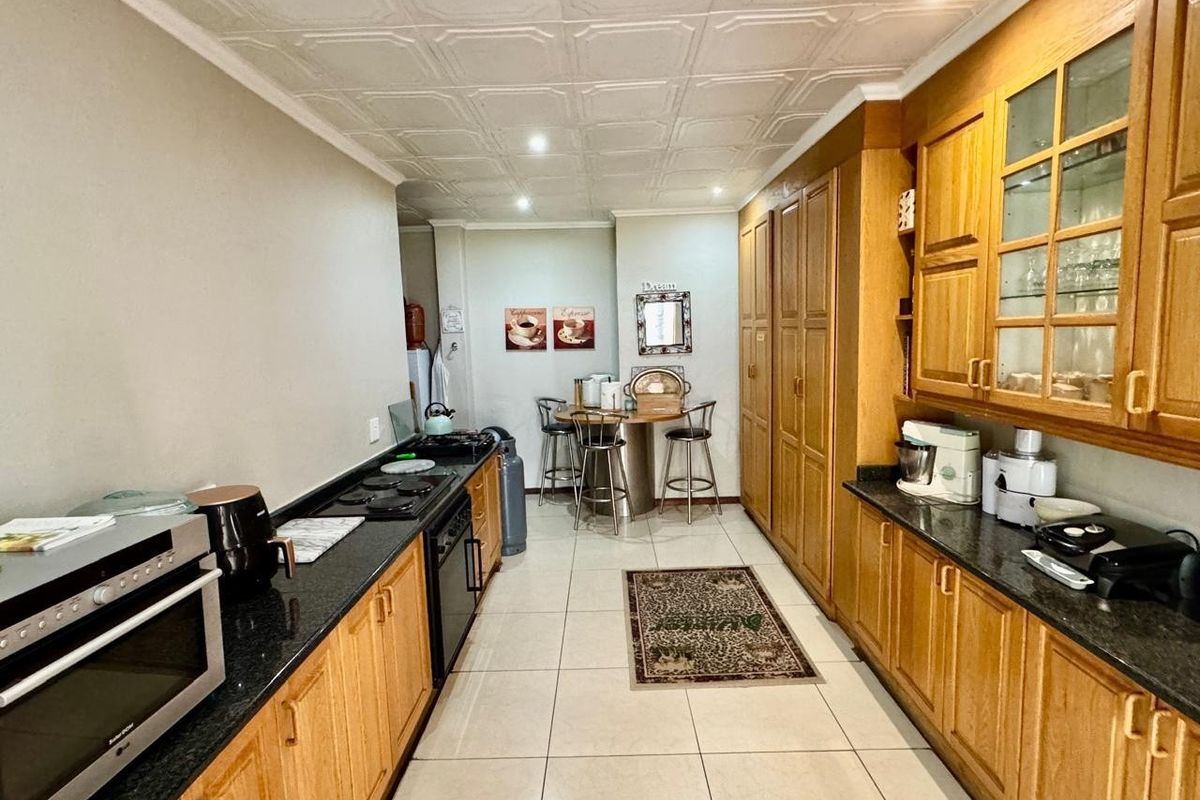 A functional kitchen featuring extensive wooden cabinetry, dark granite countertops, built-in cooking appliances, and decorative ceiling tiles with tiled flooring throughout.