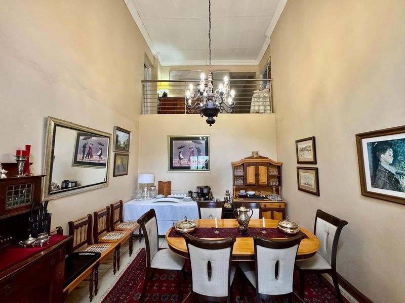 Spacious dining room featuring a high vaulted ceiling, a classic chandelier, and an open mezzanine level with a metal balustrade overlooking the area.