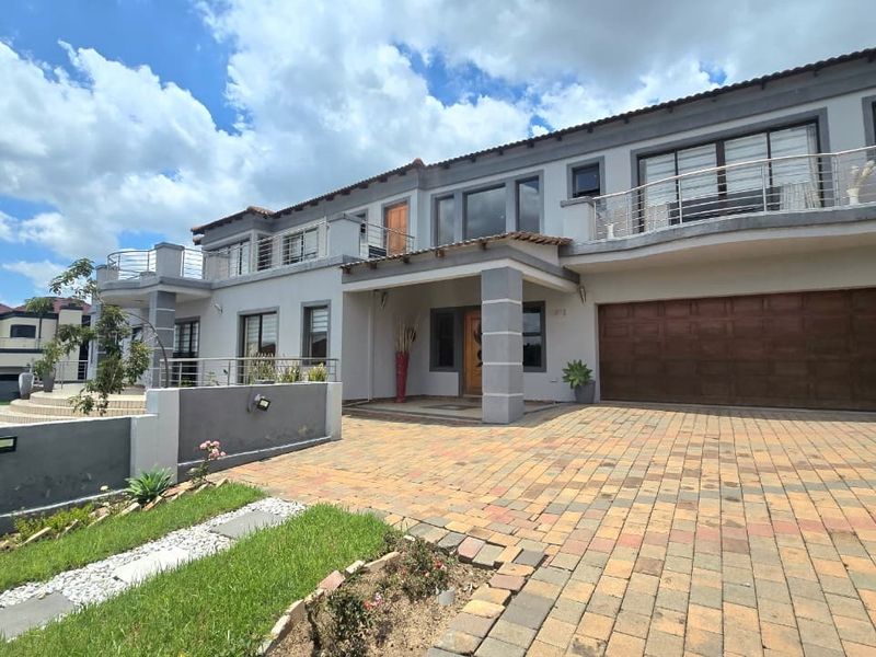 A spacious double-story residential property featuring a paved driveway, double garage, and upper-level balconies with modern stainless steel balustrades.