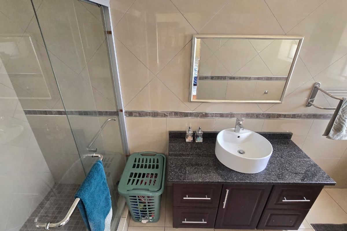 A well-maintained bathroom featuring a glass shower enclosure, dark wood vanity with granite countertop, vessel sink, and neutral wall tiling.
