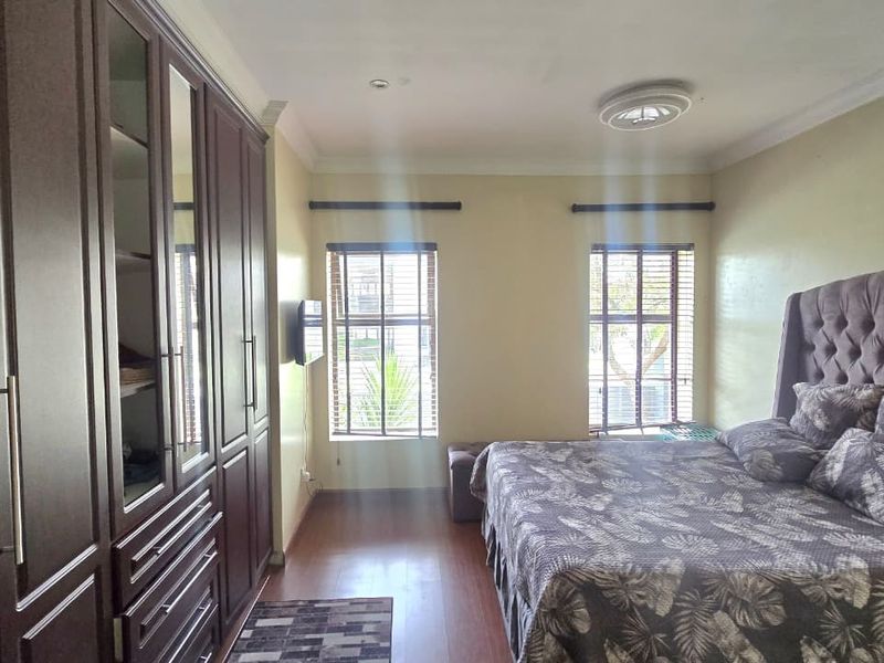 A well-maintained bedroom featuring extensive built-in dark wood cabinetry, laminate flooring, and dual windows with fitted blinds.
