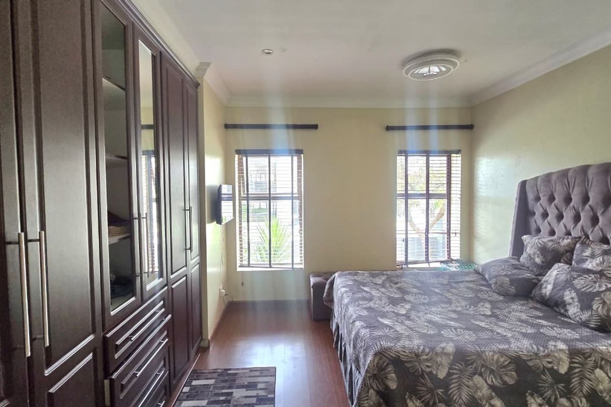 A well-maintained bedroom featuring extensive built-in dark wood cabinetry, laminate flooring, and dual windows with fitted blinds.